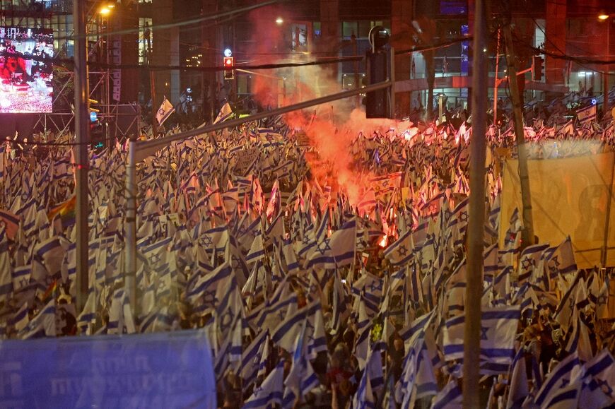 Smoke from a flare rises above a sea of Israeli flags during the latest protest