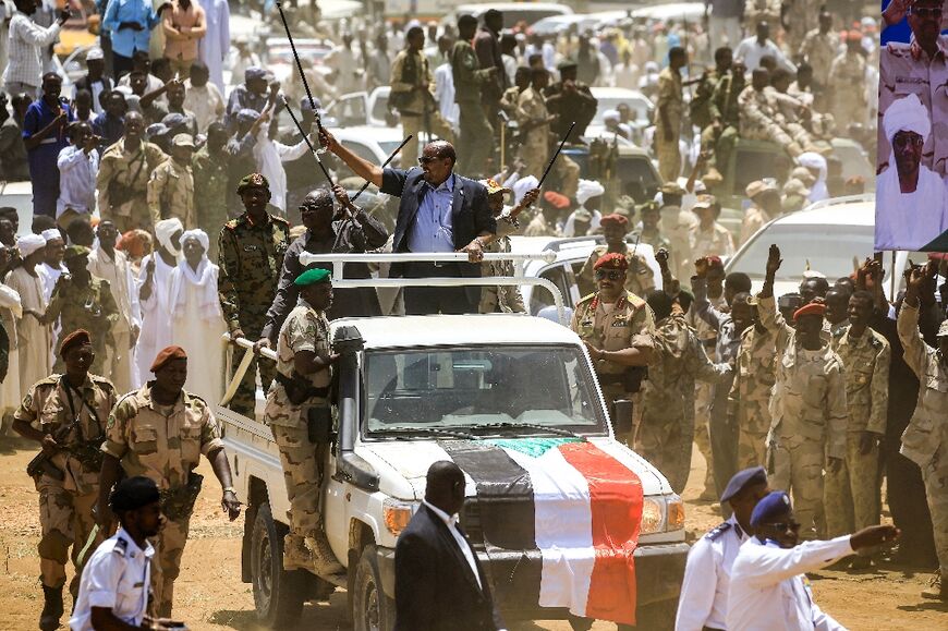 Sudanese President Omar al-Bashir (C) waves a walking stick as he tours with the commander of the Rapid Support Forces (RSF) paramilitaries Mohamed Hamdan Daglo (C-R) in South Darfur state on September 23, 2017