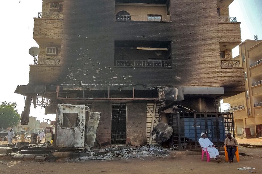 Men sit outside a burnt-out bank building in southern Khartoum on May 24, 2023
