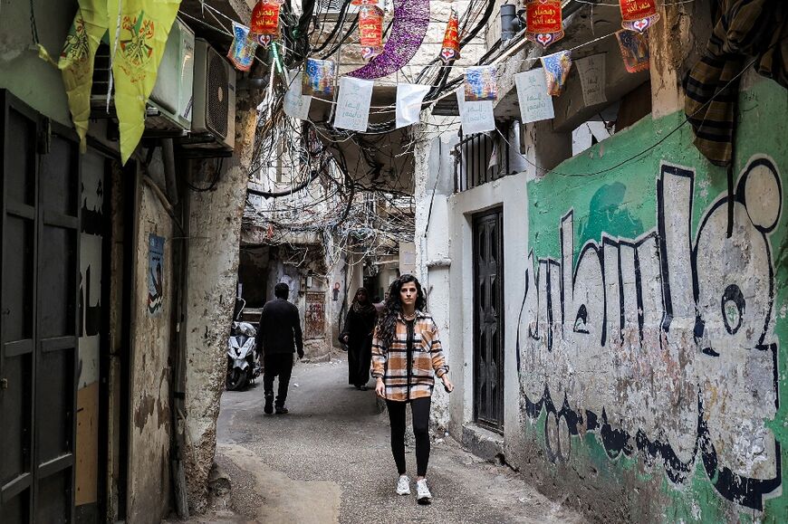 Palestinian refugee Nisreen Hazineh walks by a mural in the camp that reads 'Palestine'