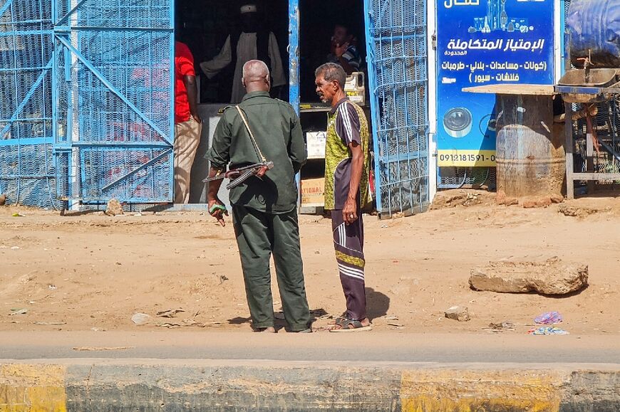 A member of the Sudanese army speaks to a man in front of open shops in southern Khartoum