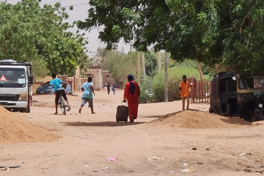 A woman rolls her suitcase on a dirt road in southern Khartoum, at the end of the latest breached ceasefire between Sudan's warring generals