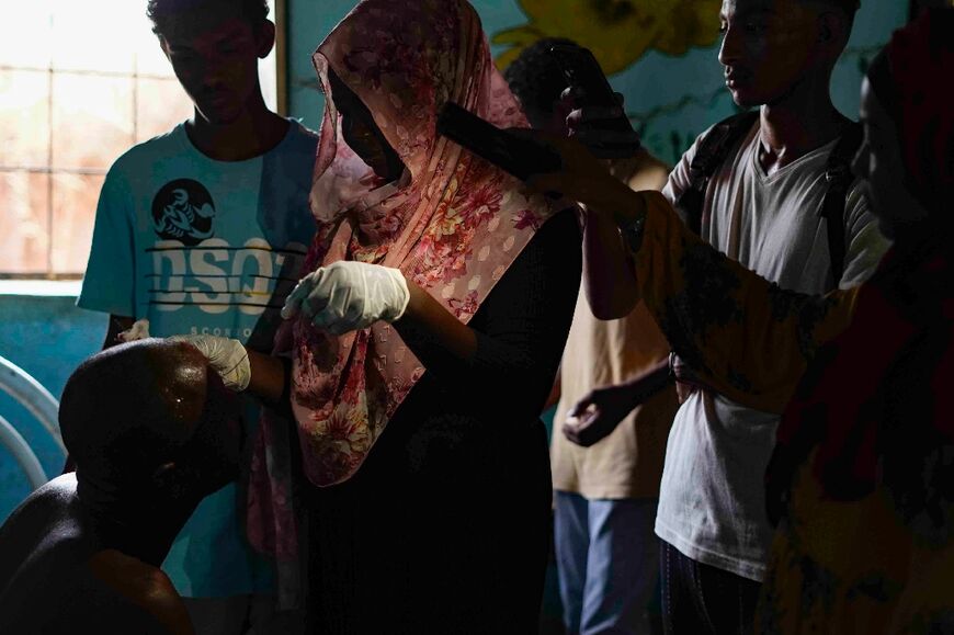 With electricity out and medical services severely disrupted, people use the flashlights on their phones to assist a woman stitching a man's head in Khartoum's twin city Omdurman