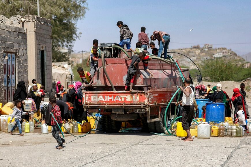 People gather with jerrycans to fill up water from a tanker truck on the outskirts of Yemen's third city of Taez, on June 8, 2023
