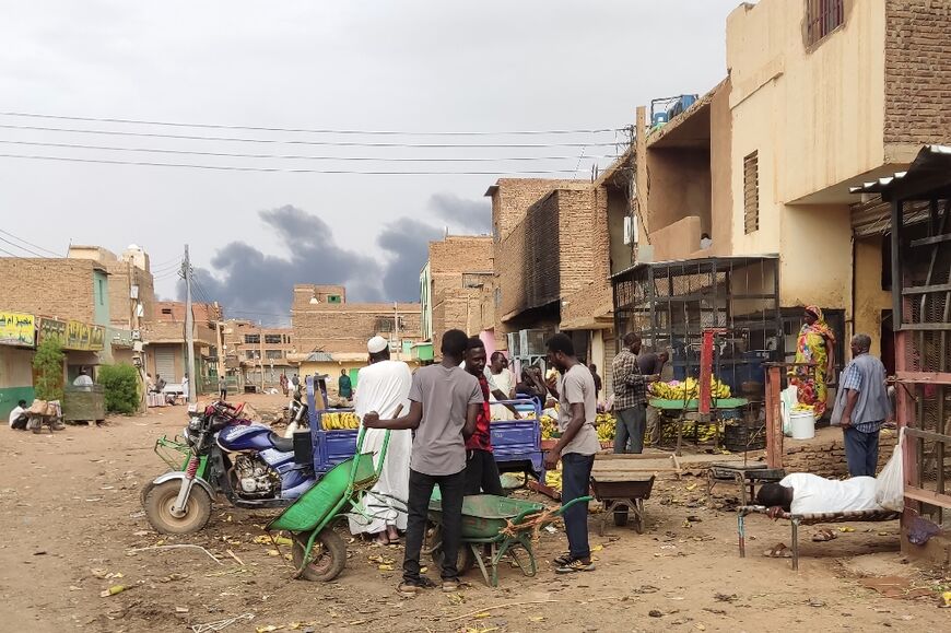 Smoke rises above buildings as people gather at a market to buy food, in Khartoum on June 10, 2023