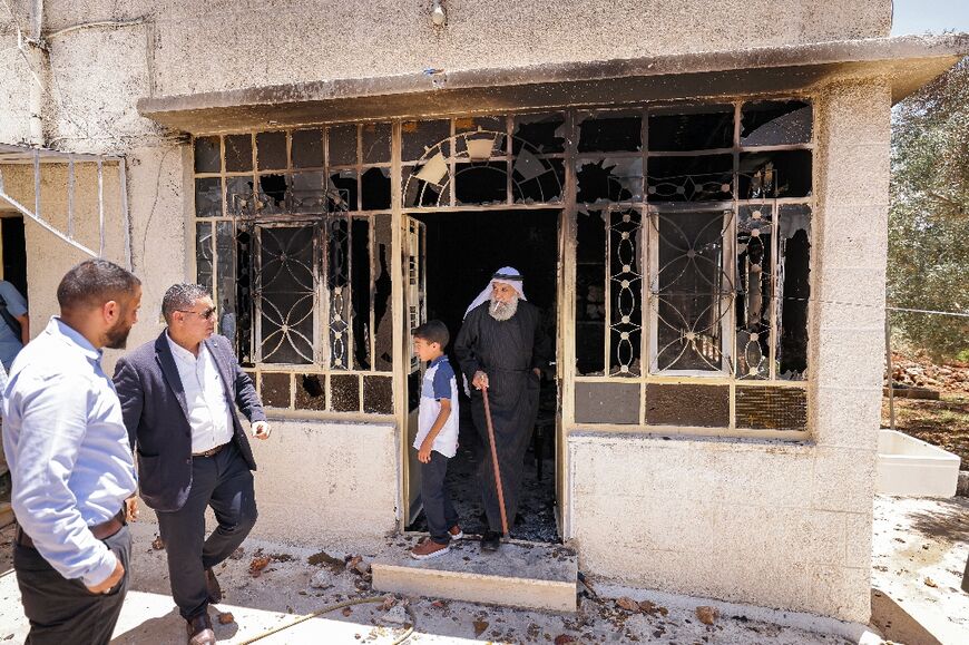 Palestinians watch on from the doorstep of their burnt-out home as foreign diplomats tour the village of  Turmus Ayya
