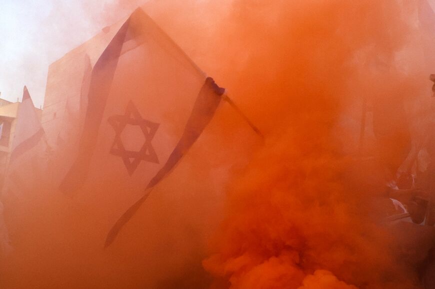 An Israeli flag flown by a demonstrator is surrounded by smoke from flares during a protest against the Israeli government's judicial overhaul bill