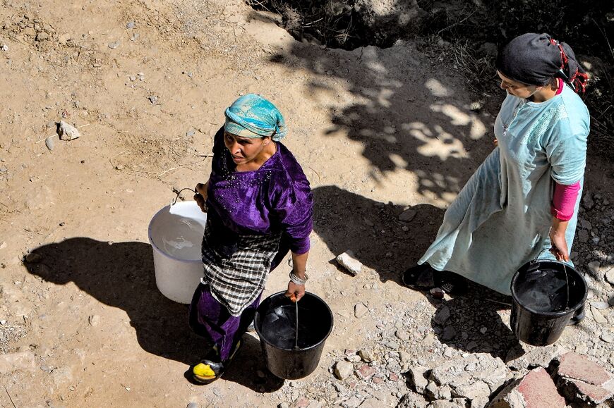 Women walk with buckets of water after pipes were broken and springs blocked by the quake