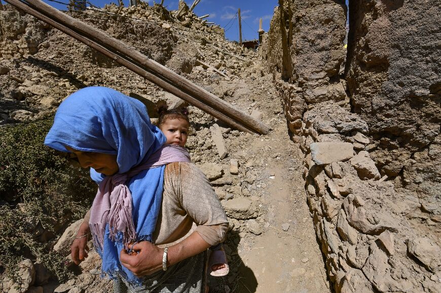 A woman carrying a child on her back walks amid the rubble of the village 