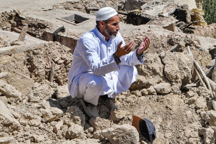 A man prays as he sits on the rubble of a destroyed building