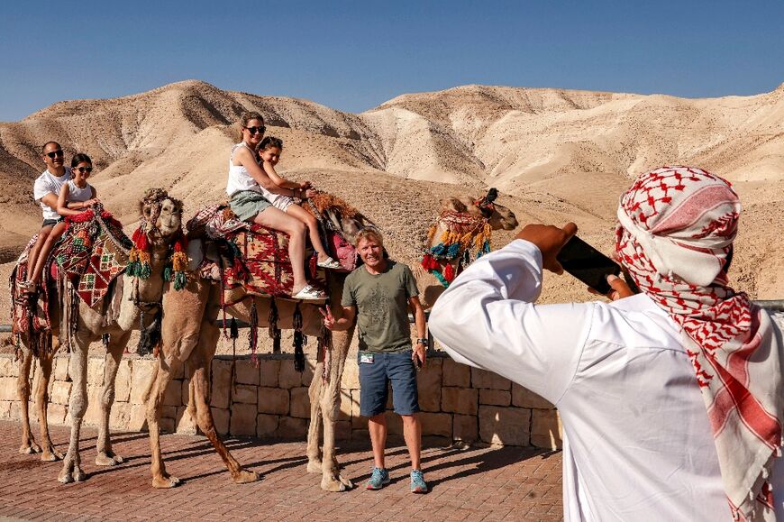Tourists get their picture taken while riding camels near the sign marking mean sea level, along the road between Jerusalem and the Dead Sea south of Jericho