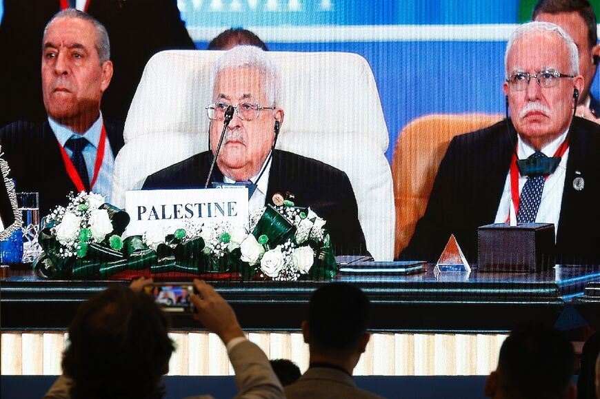 Journalists watch a large screen showing Palestinian President Mahmud Abbas attending the International Peace Summit hosted by the Egyptian president in Cairo  