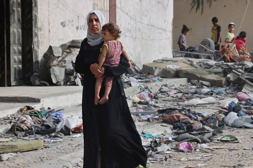 A Palestinian woman carries a child as she walks through debris in Gaza's residential neighbourhood of Rafah, following Israeli airstrikes on the southern Gaza Strip 