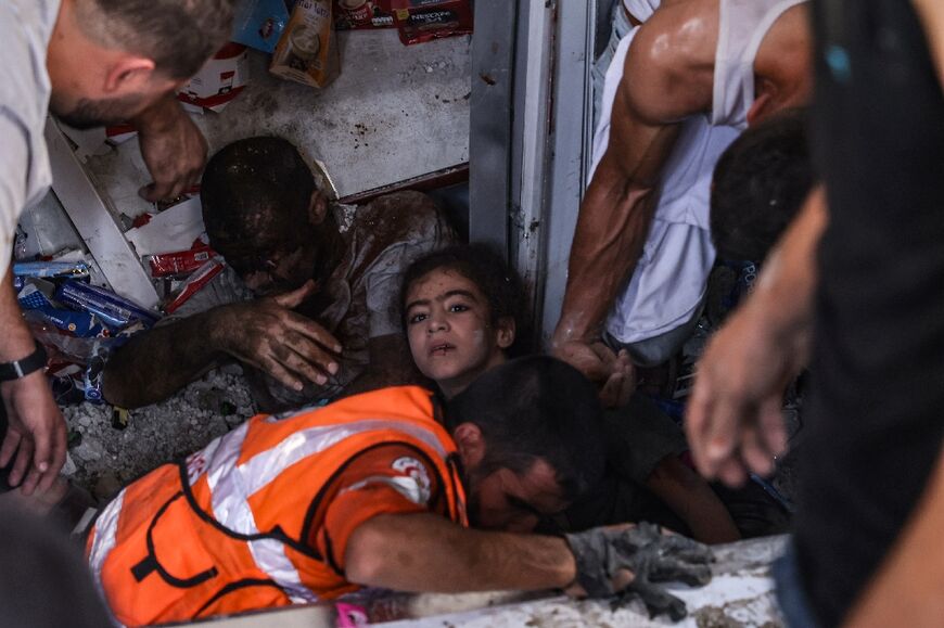 Rescuers pull out an injured girl and a man from under the rubble of a supermarket hit by an Israeli strike on the Rafah refugee camp in the southern Gaza Strip on October 25, 2023