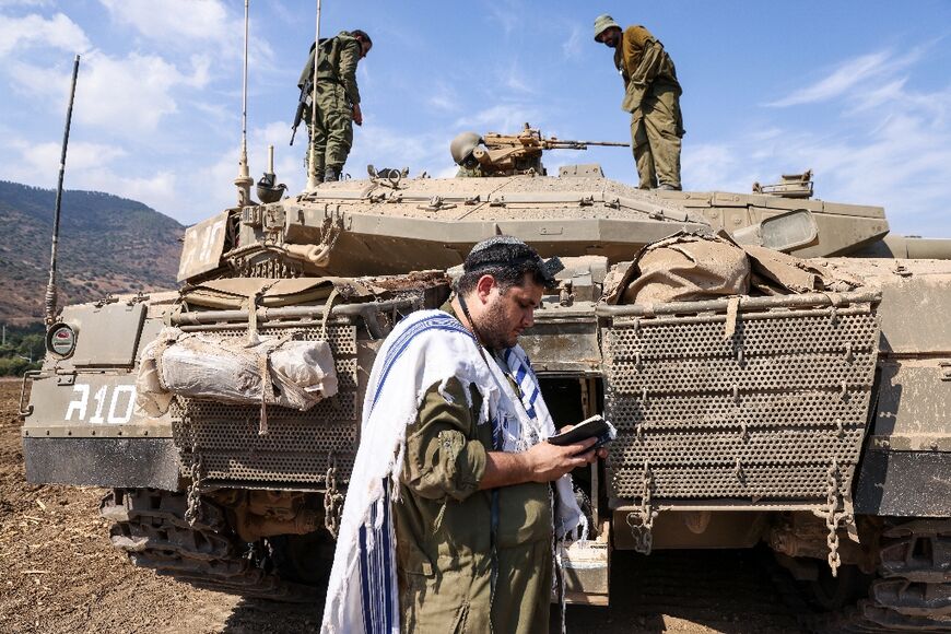 An Israeli soldier prays in front of a Merkava tank near the the northern town of Kiryat Shmona, close to the border with Lebanon, on October 8, 2023