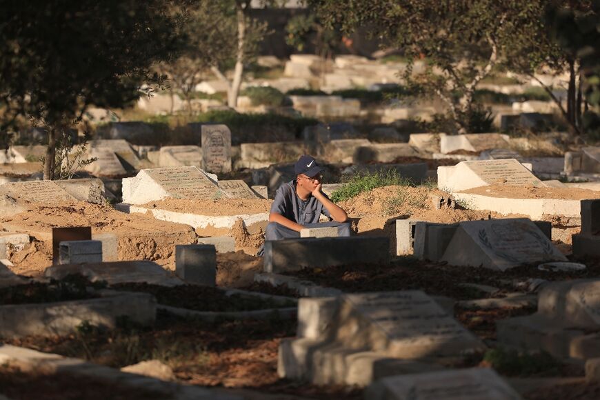 A Palestinian man sits next to graves at the Deir el-Balah cemetery in the central Gaza Strip