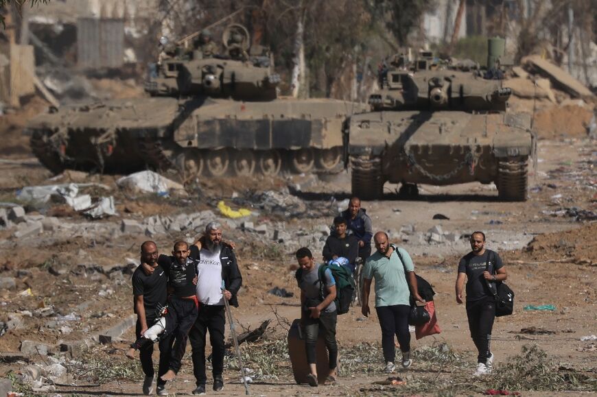 Palestinians fleeing the north along Salaheddine road help a man with a bandaged leg as they walk in front of Israeli army tanks on the southern outskirts of Gaza City