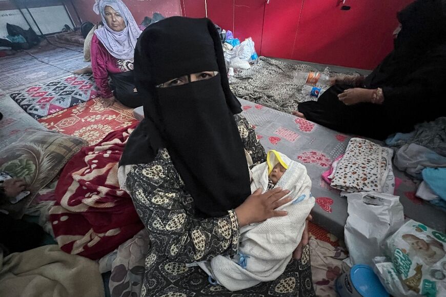 A Palestinian woman carries her newborn son at a UN-run shelter in Rafah in the southern Gaza Strip