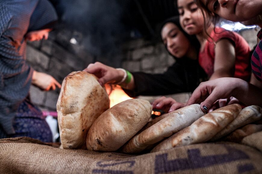Children reach for a loaf of bread freshly-baked in a clay oven in a home in Khan Yunis