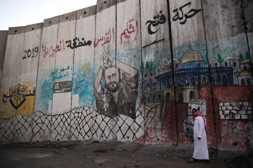 A Palestinian man in the West Bank town of al-Azariya walks alongside Israel's separation barrier painted with an image of Marwan Barghuti, the best-known Palestinian prisoner detained by Israel