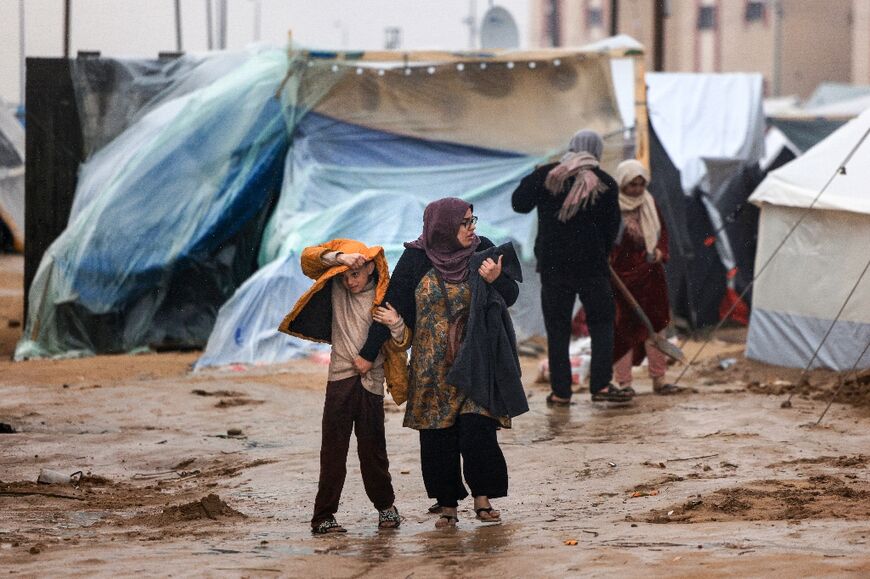 Palestinians walk under the rain at a camp for displaced people in Rafah, in the southern Gaza Strip where most civilians have taken refuge, on December 13, 2023
