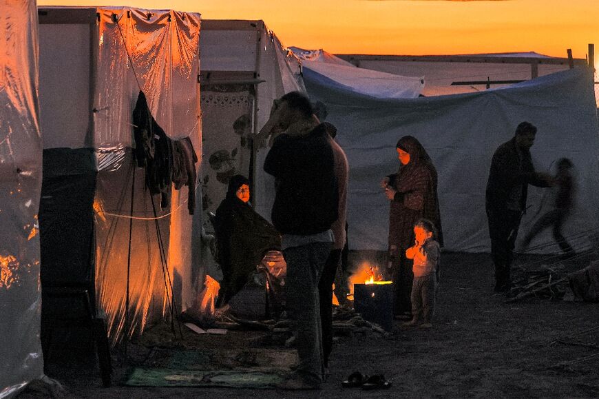Men pray at sunset as people sit by a fire outside one of the tents housing Palestinians displaced by the conflict 