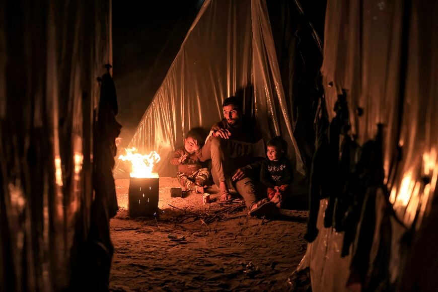 A man sits with children by a fire outside one of the tents housing Palestinians displaced by the conflict in  Rafah in the southern Gaza Strip on December 18, 2023