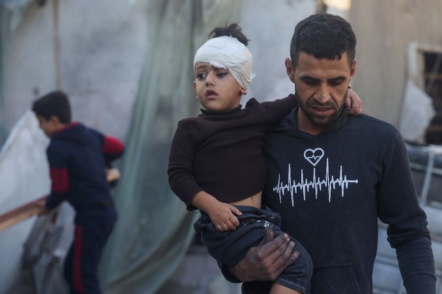 A Palestinian man carries a child injured during Israeli bombardment in Rafah