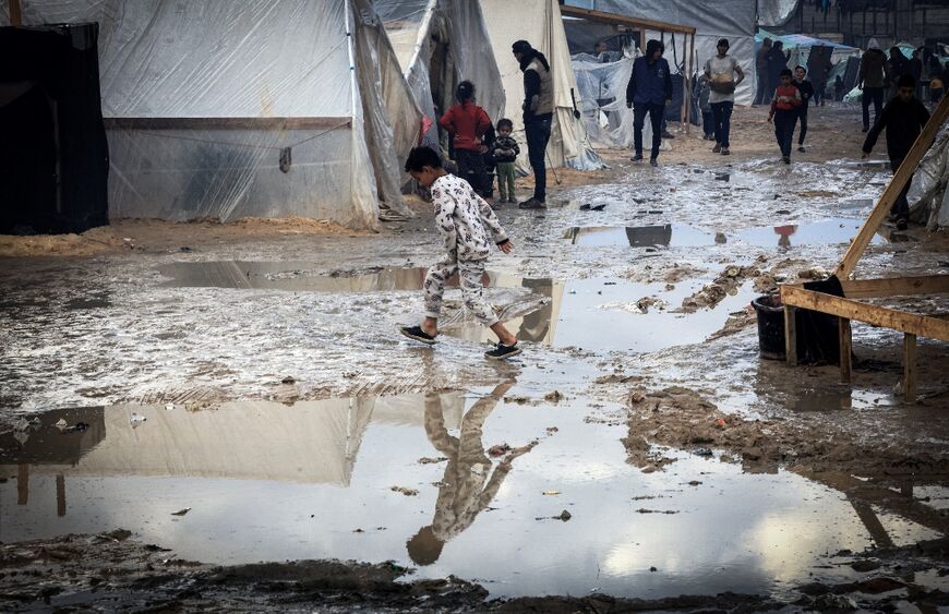 A Palestinian child walks on a muddy path past tents at a makeshift camp in Rafah 
