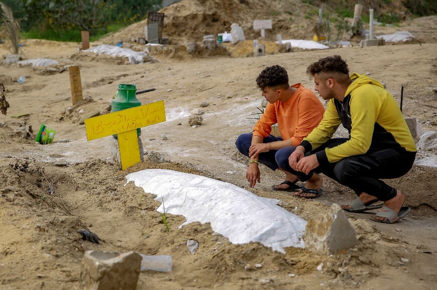 Young men visit a shallow grave at a makeshift cemetery in Gaza City
