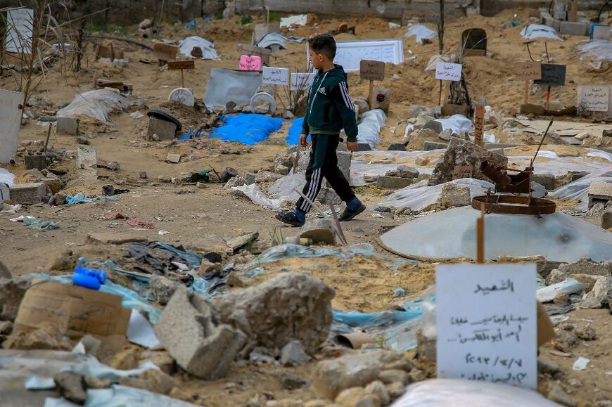 A Palestinian boy walks past graves at a makeshift cemetery in Gaza City's Al-Sahaba Street