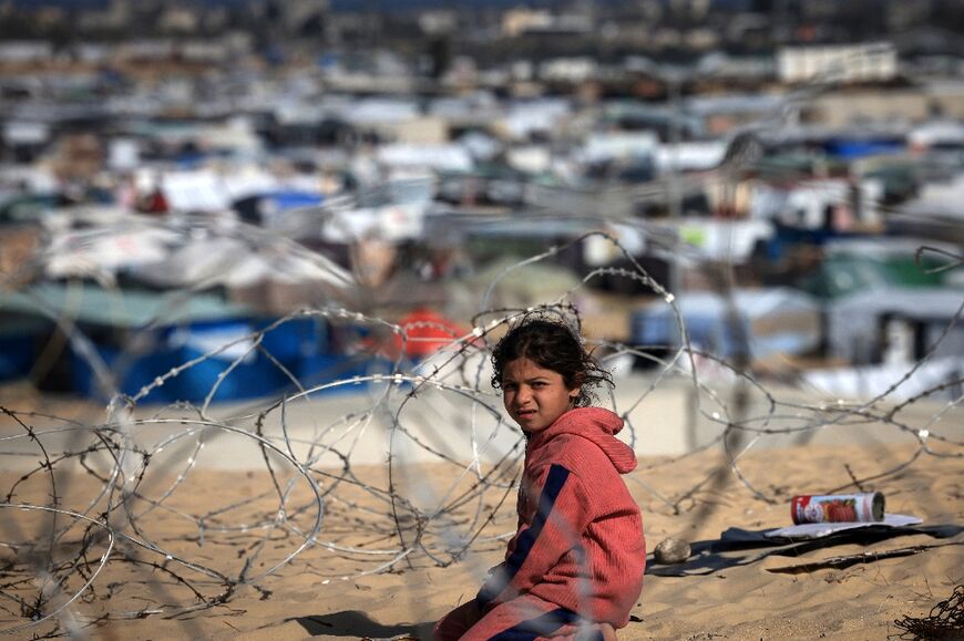 A displaced Palestinian child sits behind barbed wire on a dune overlooking a makeshift camp on the Egyptian border, west of Rafah in the southern Gaza Strip 