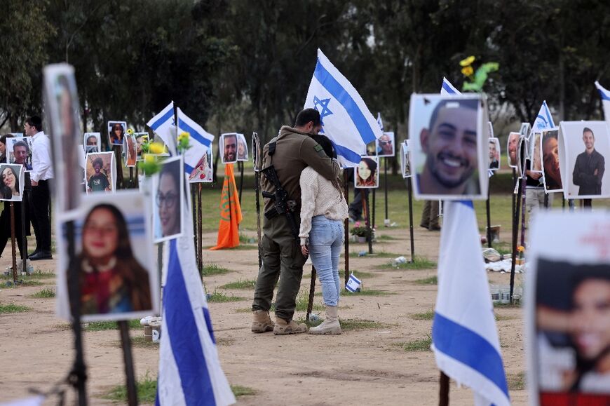On the 100th day of the war, an Israeli soldier hugs a woman among national flags and portraits of Israelis taken captive or killed by Hamas militants, near Reim, southern Israel