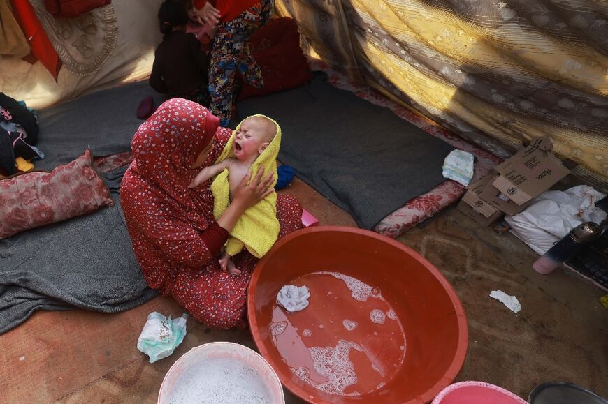 A woman dries a baby after bathing it inside a tent at a camp for displaced Palestinians in Rafah, the southern Gaza Strip, where many people have fled