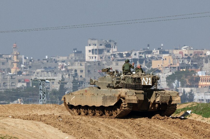 An Israeli tank, photographed from southern Israel, overlooks damaged buildings in the Gaza Strip