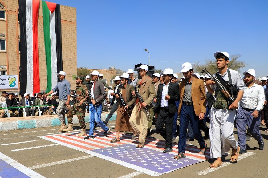 Students recruited into the ranks of Yemen's Huthi rebels hold automatic rifles as they parade over a US flag during a rally in Sanaa on February 21, 2024 
