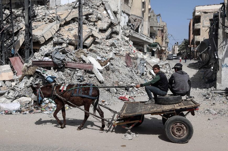 Palestinian boys ride a donkey cart near a building destroyed in Israeli bombardment in Rafah in the southern Gaza Strip on March 31, 2024