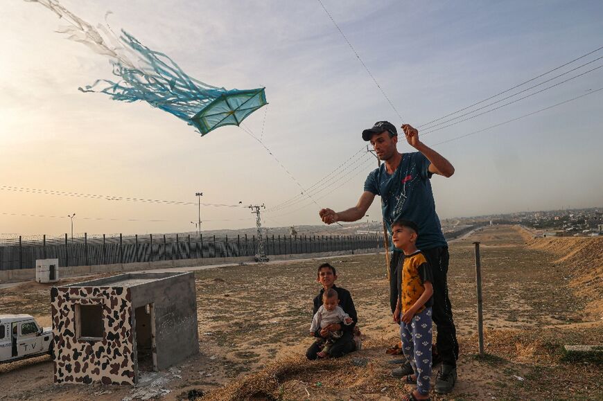 A displaced Palestinian man helps a child fly a kite near the border with Egypt in Rafah