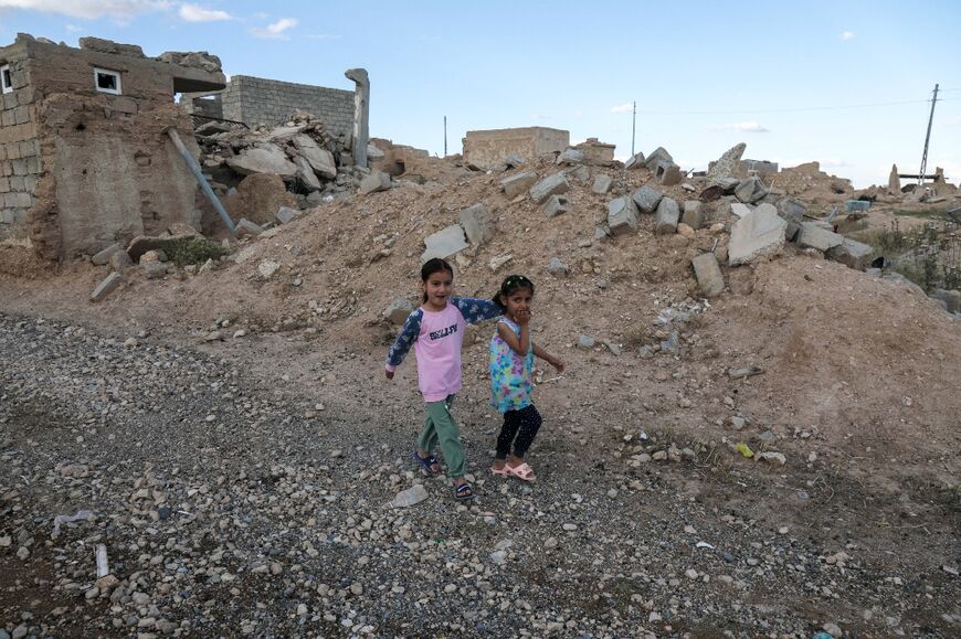 Iraqi Yazidi children walk near buildings that were destroyed during the 2014 attack by Islamic State group