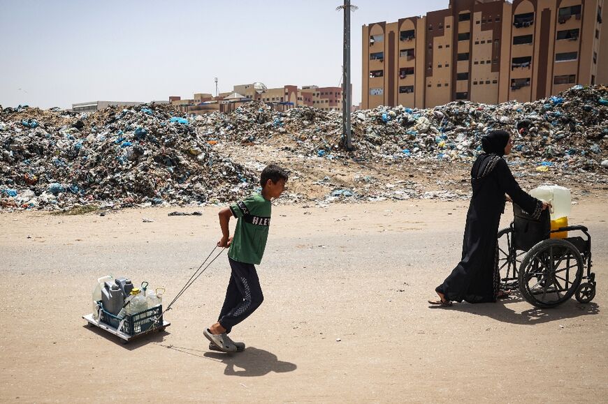A child and a woman transport water as they walk past garbage piled up near tents set up by displaced Palestinians in Khan Yunis 