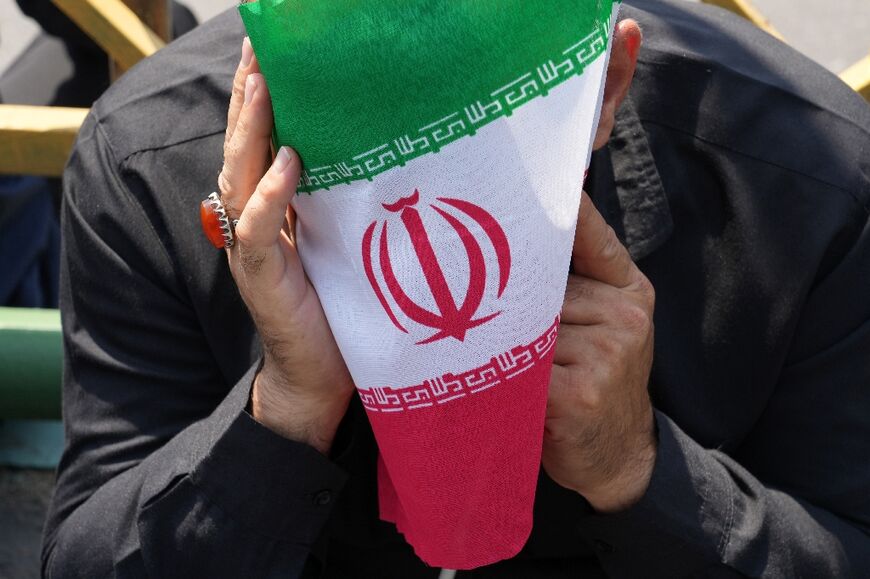 An Iranian mourner covers his face with a national flag during the funeral procession of president Ebrahim Raisi in Tehran