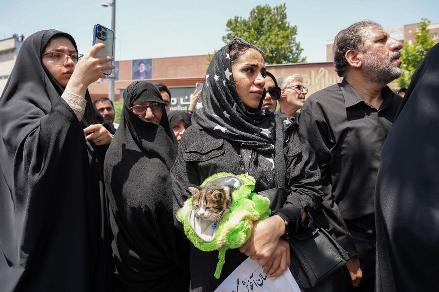 A woman holds her cat as she joins the crowds attending Raisi's funeral