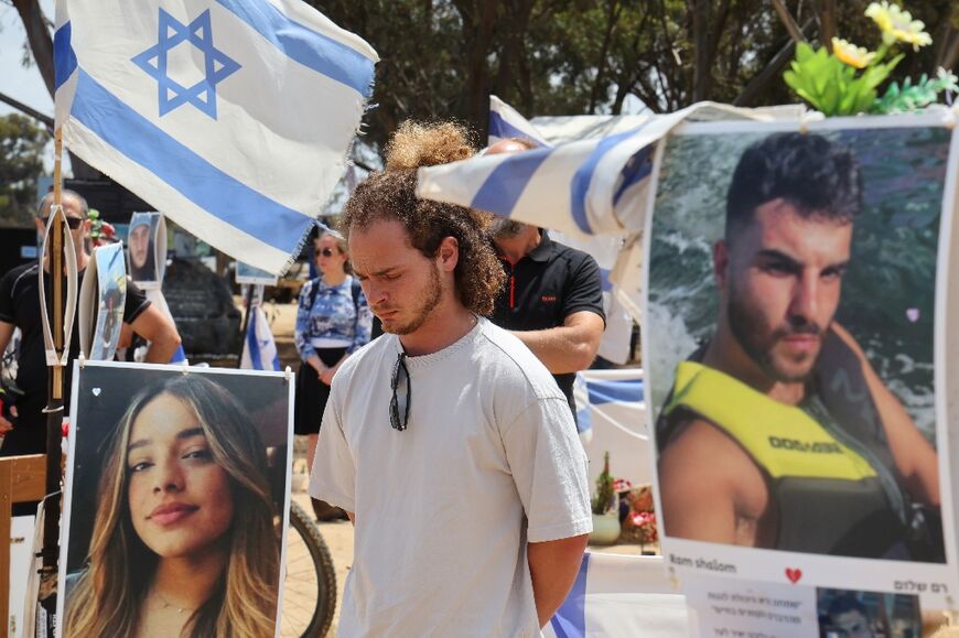 Mourners stand next to portraits of Israeli hostages held by Hamas as they observe two minutes of silence on Yom HaZikaron (Memorial Day) near southern Israel's Kibbutz Reim on May 13, 2024, at the site of the Supernova music festival 
