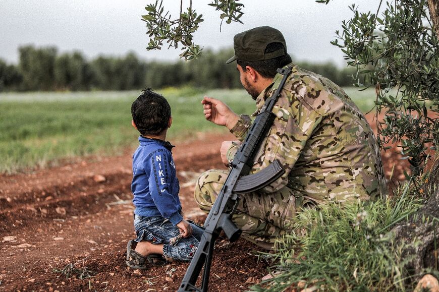 Ahmed, a 30-year-old pro-Turkish Syrian fighter, sits with his son in a field in Aleppo province