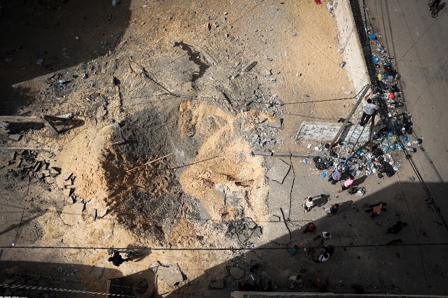 People gather around a crater caused by Israeli bombardment in a street in Rafah in the southern Gaza Strip on May 18, 2024