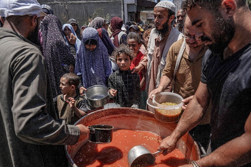 People are handed food portions from a large pot at a public kitchen in Deir el-Balah in the central Gaza Strip