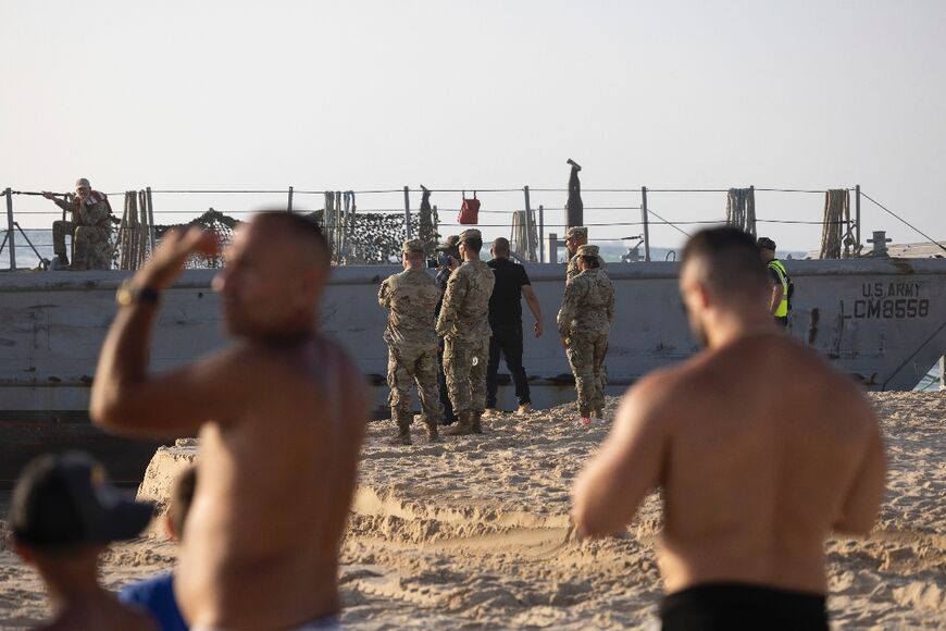 Israeli beachgoers look on as US soldiers supporting the Gaza aid pier stand near a military vessel that ran aground
