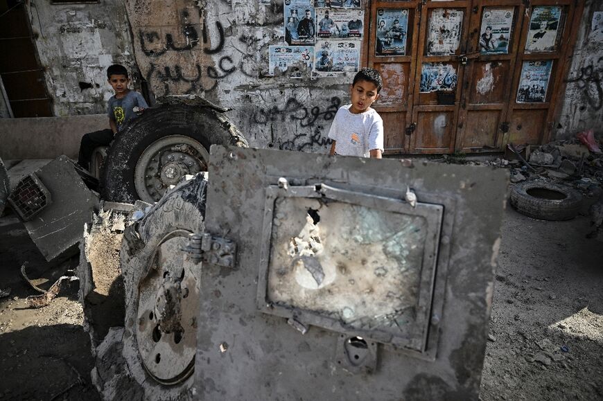 Palestinian children stand behind a destroyed vehicle in Jenin in the aftermath of a raid by Israeli forces