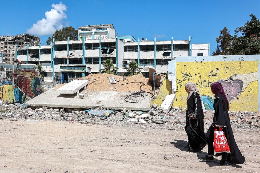 Women walk past the destroyed wall of a school for boys run by the UN agency for Palestinian refugees (UNRWA)