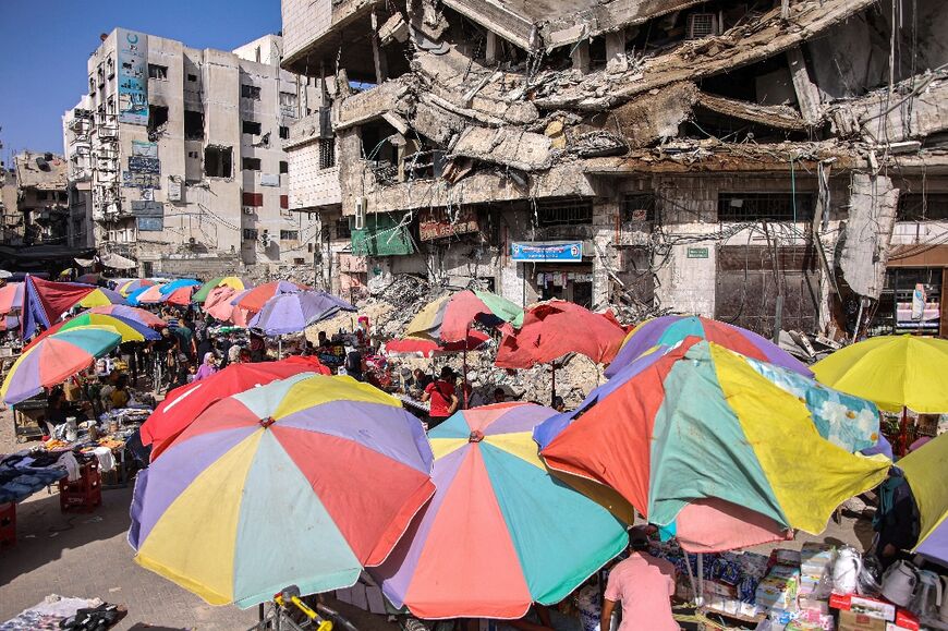 Vendors' umbrellas shade their stalls while erected before destroyed buildings along a market street in Gaza City